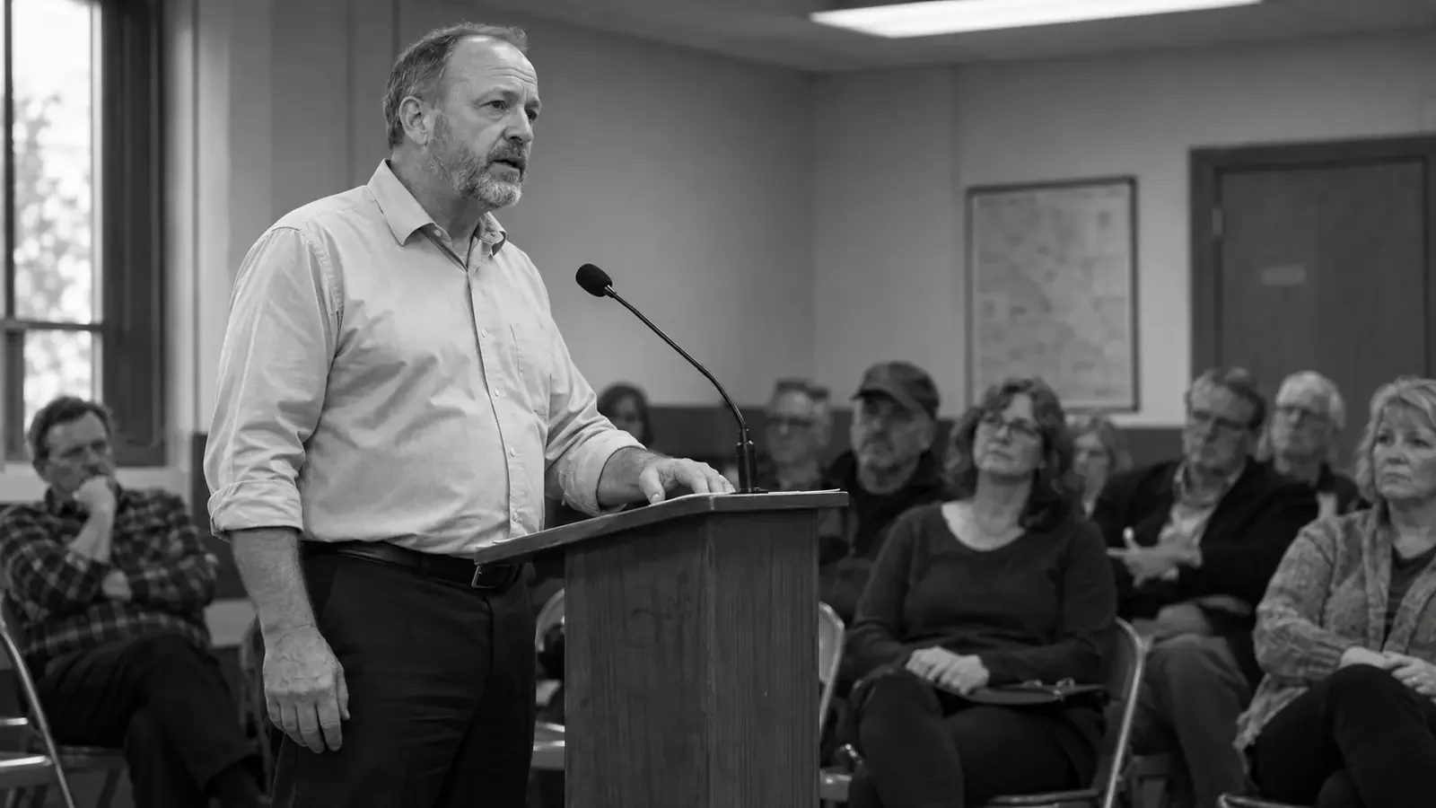 A man speaks at a lectern in a community meeting room
