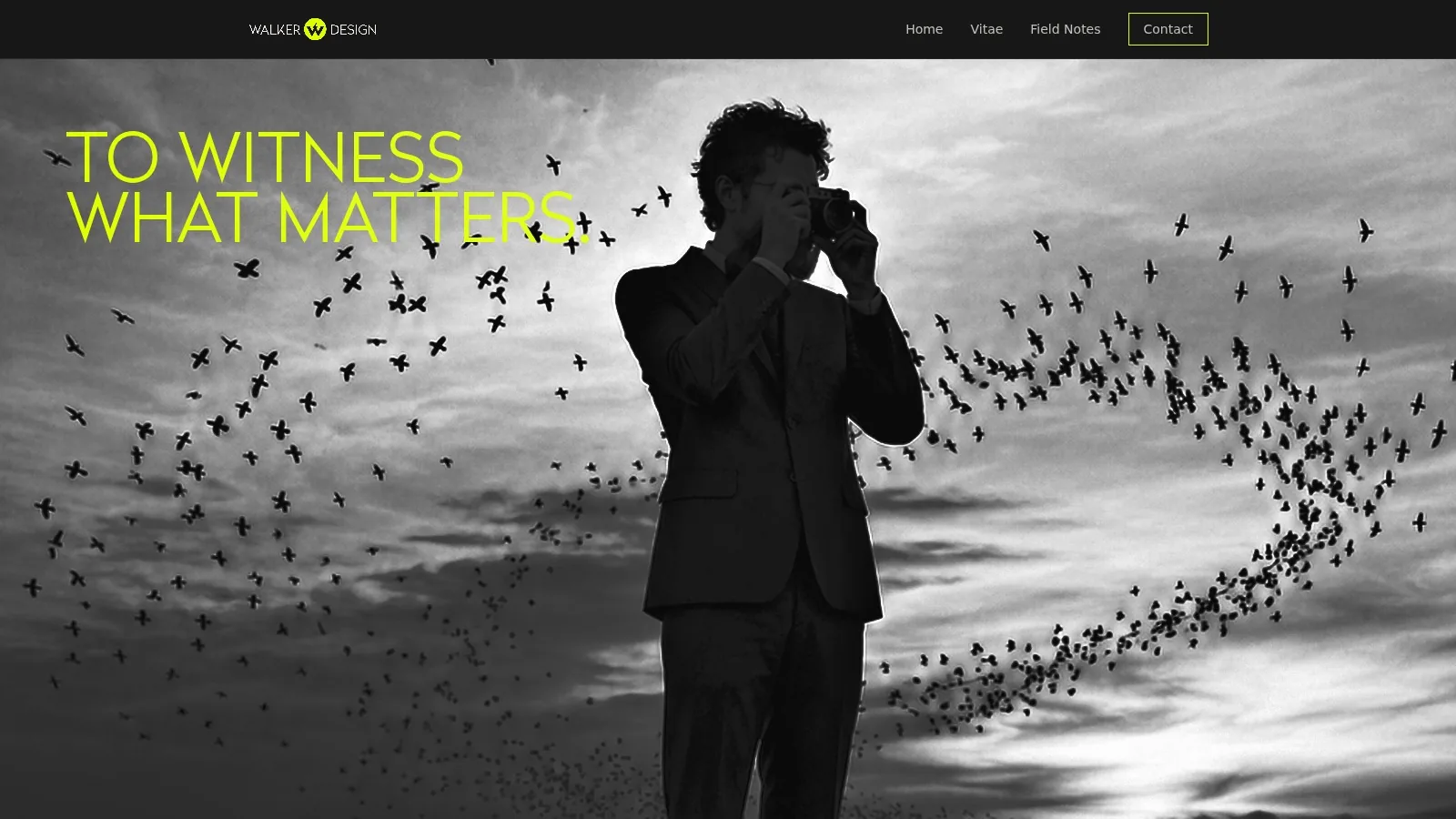 A man photographing a murmuration of birds above a shoreline at dusk, in black and white.